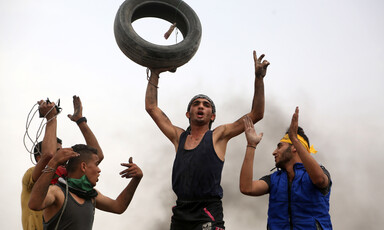 Young man holds tire above his head as other protesters clap and celebrate around him