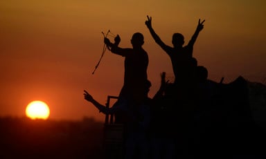 Silhouettes of protesters making V for victory signs and holding slingshots are seen against a setting sun