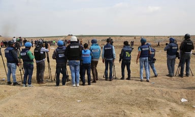 Palestinian journalists wearing press vests stand in a row at the Gaza march. 