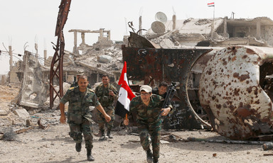 Men in military uniform carry Syrian flag amid rubble of bombed-out buildings