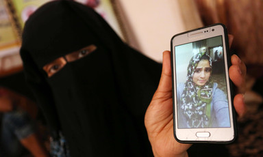 Woman wearing niqab displays photo of adolescent girl wearing a hijab on a mobile phone