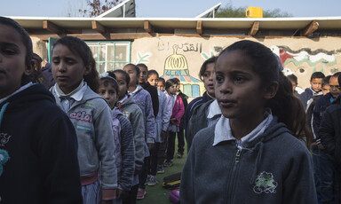 Schoolchildren stand in rows in front of single-story school