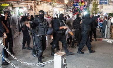 Security forces carrying rifles and wearing all black and face masks walk through city center