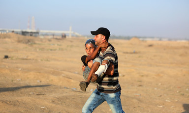 A man carries a boy with a bandaged leg across a sandy landscape