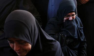 Photo shows two mourning women wearing black headscarves and dresses