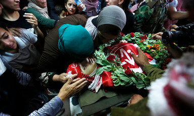 Women and girls mourn over body of youth wrapped in PFLP flags with a wreath placed on his torso