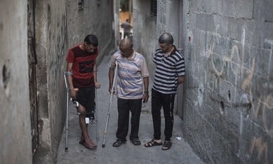 Three men stand in an alley, two of them using crutches.