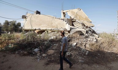 A man holding a cigarette walks past a collapsed building