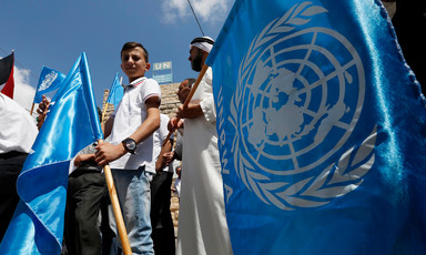 Man and boy are seen from legs up holding UN flags