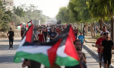Palestinian men and boys march down street while carrying Palestinian flags