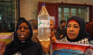 Palestinian women holding up a bottle reading "water and salt." 