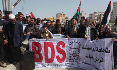 Crowd holds Palestinian flags and large banner reading BDS in English and spelling out boycott, divestment and sanctions in Arabic