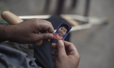 Close-up photo of two hands holding a passport-size image of a smiling baby