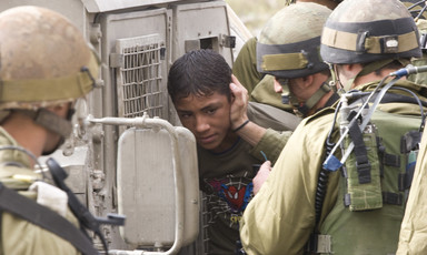 A group of Israeli soldiers put a boy wearing a Spiderman T-shirt into a military jeep