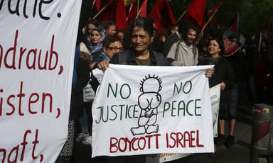 A woman holds a banner reading No Justice No Peace Boycott Israel amid crowd