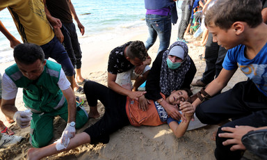 Men and women provide first-aid to a child lying on the beach with a bandage on his leg 
