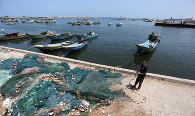 A young man pulls on a pile of fishing nets while standing next to docked boats