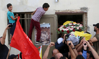 A boy stands on a windowsill, leaning on a door, as the shrouded body is carried out of a home