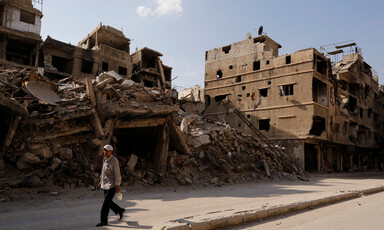 Man walks down street with ruins of multi-story buildings behind him