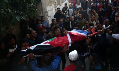 The body of Muhammad Habali, wrapped in a Palestine flag, is carried on a stretcher by crowd in alley