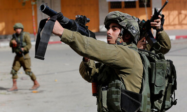 Two Israeli soldiers point their weapons at Palestinian demonstrators.