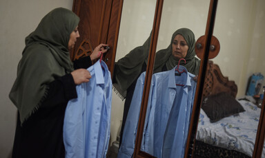 Woman holds shirt, while looking into mirror