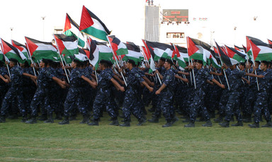 Young men wearing camouflage uniforms and berets carry Palestine flags while marching during graduation ceremony