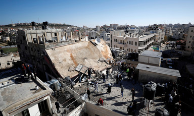 Landscape view of people standing on rooftops adjacent to destroyed building