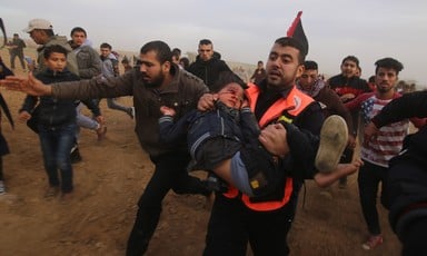 A paramedic carries a small child with blood splattered around his eye as others run alongside them