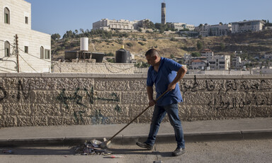 A man pushes trash with a broom along a street