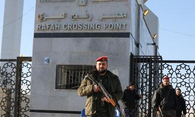 Men in military uniform carrying rifles stand in front of Rafah crossing gate