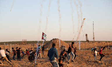 Palestinians protest in front of Gaza boundary fence with trails of tear gas smoke in the sky