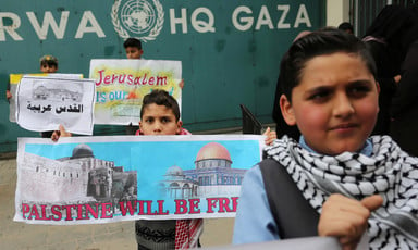 Children standing in front of UNRWA headquarters in Gaza hold signs saying Palestine Will be Free and Jerusalem is Our Land