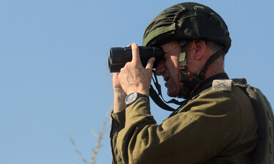 A man in military uniform looks through binoculars