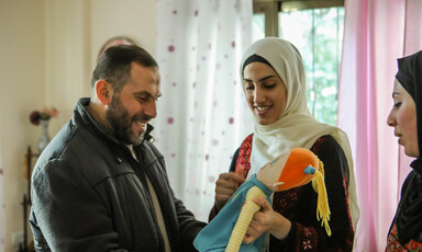 A smiling Imad al-Din al-Saftawi looks at a plush doll held by a smiling young woman