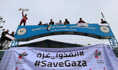 Banner reading #SaveGaza in English and Arabic hangs across checkpoint gate