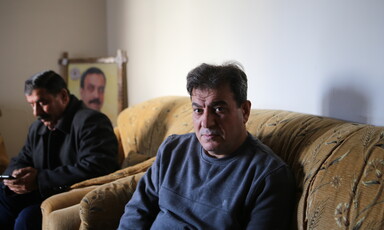 Man sitting on couch facing camera is seen from waist up