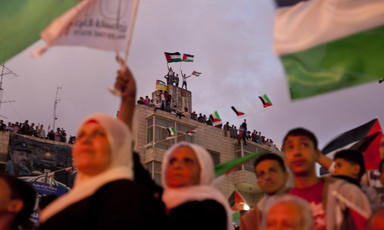 Crowd of people wave Palestinian flags, including from rooftop