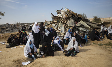 Women sit in front of ruins of demolished home. 