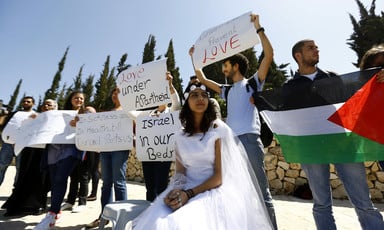 A young woman in a bridal grown sits in front of protesters holding signs