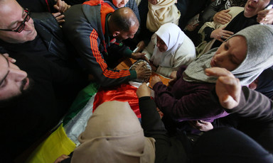 Men and women crowd around body shrouded in Palestine flag