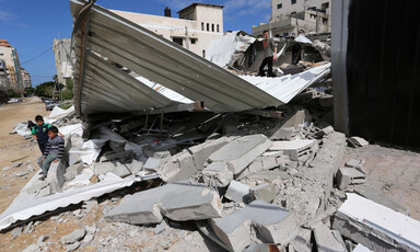 Young people sit and walk across rubble of destroyed structure
