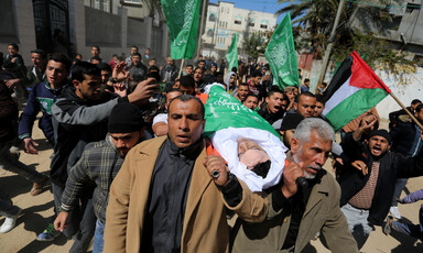 Walking men carry a body on a stretcher wrapped in a flag