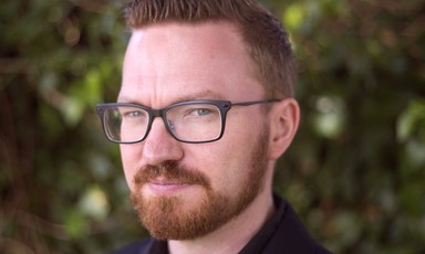 A man with a red beard, dressed in a black shirt wearing glasses.