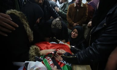 People stand and kneel around body shrouded in Palestine flag