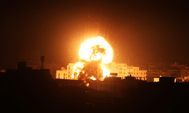 A massive fireball rises over high-rise buildings against a night sky