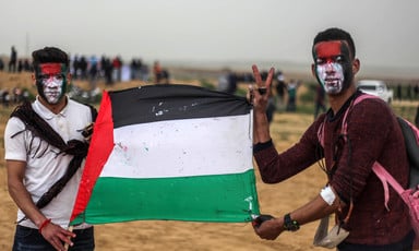 Two young men with painted faces hold a Palestinian flag
