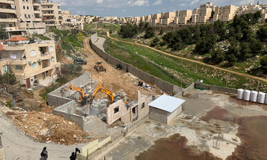 Hyundai bulldozers demolish home amid buildings and fields. 