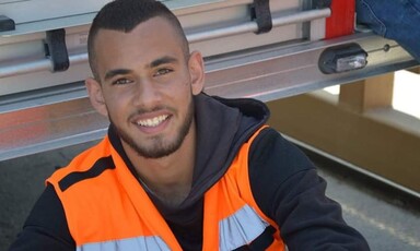 Smiling young man wearing black hoodie and high-visibility vest is seen from chest up