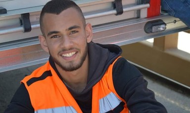 Smiling young man wearing black hoodie and high-visibility vest is seen from chest up
